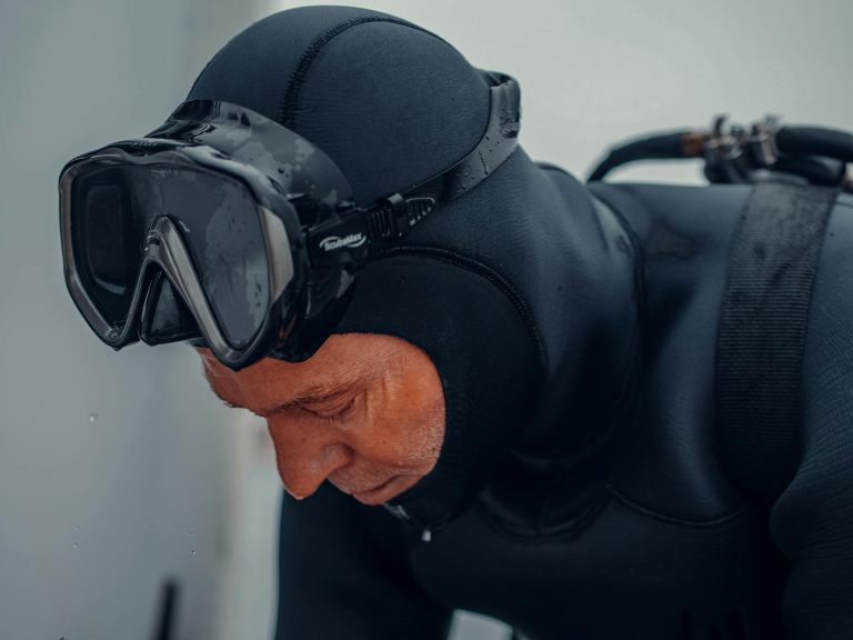 A close-up of a scuba diver in a wetsuit adjusting gear before a dive.
