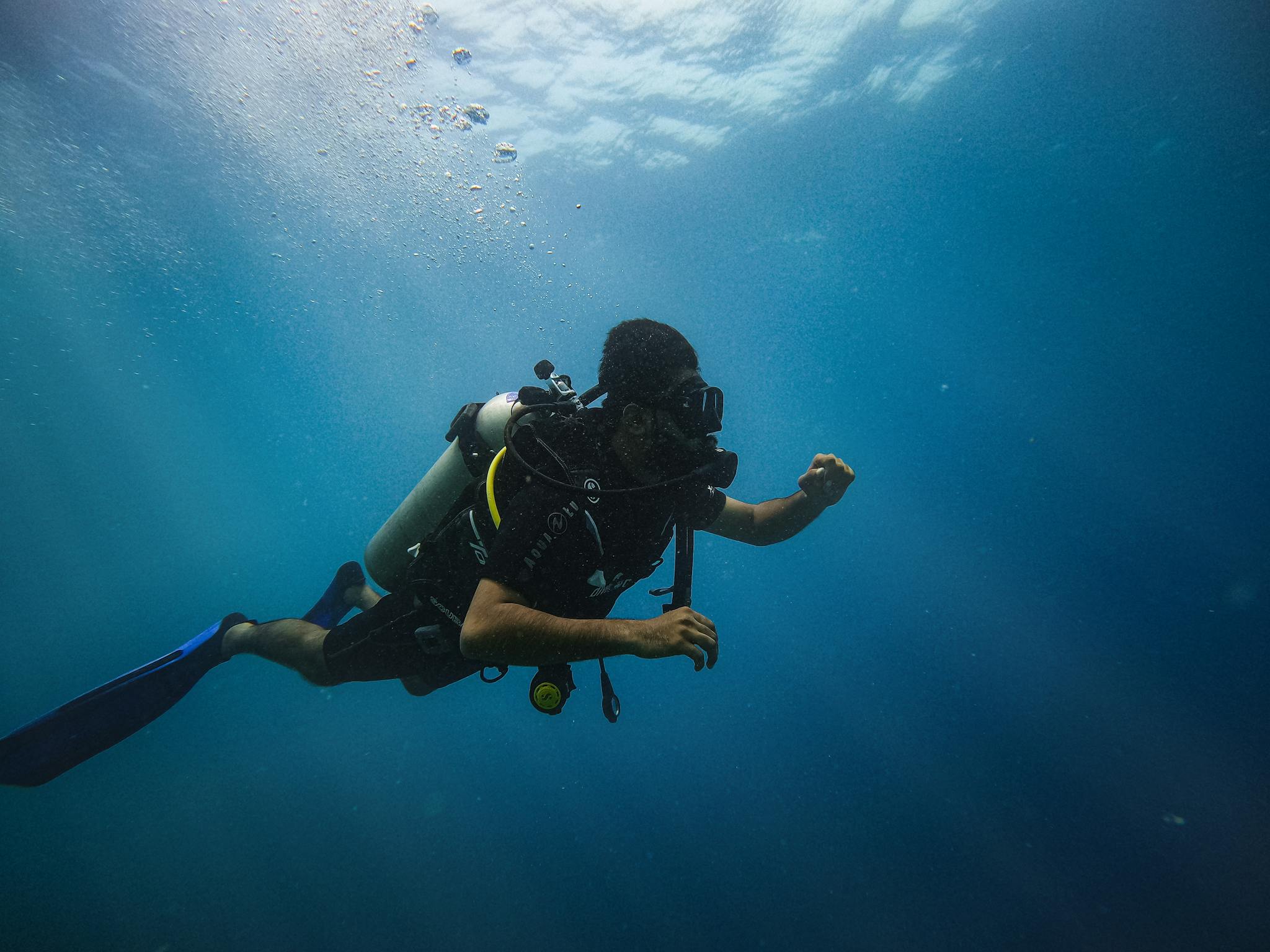 A scuba diver in full gear swimming underwater in the ocean, surrounded by a calm blue sea.