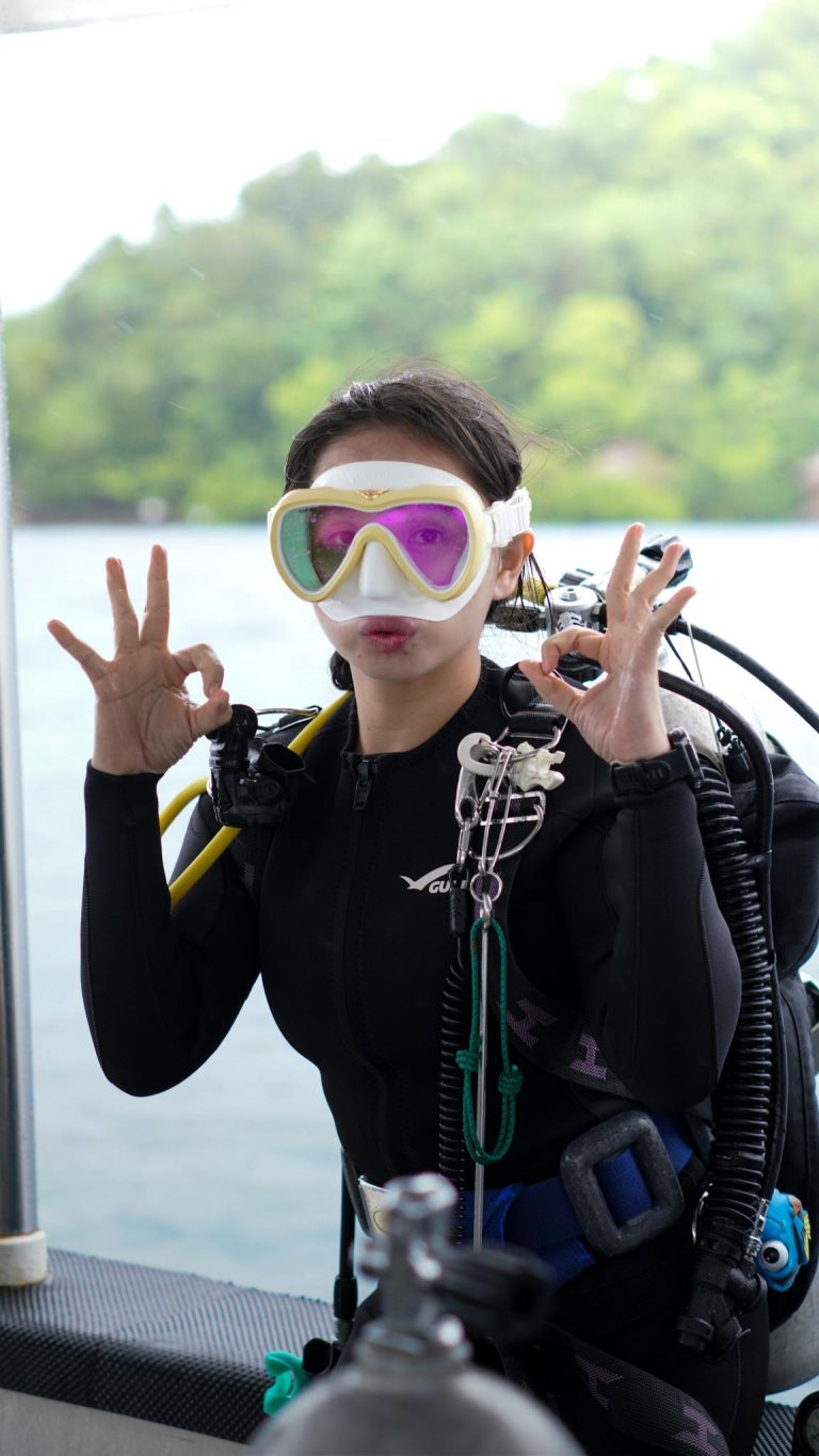 Female scuba diver signaling OK in diving suit and gear on a boat.