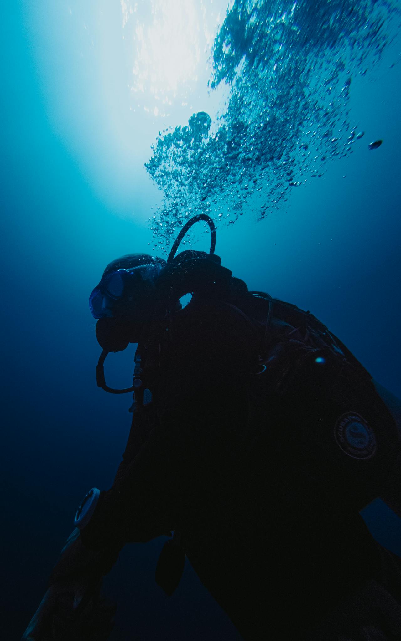 Scuba diver exploring the deep blue ocean beneath sunlight, bubbles rising.